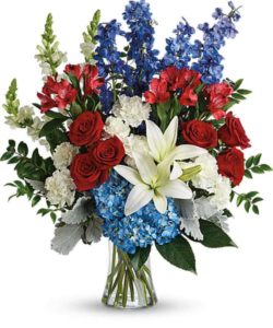 blue hydrangea, red roses, white asiatic lilies, red alstroemeria, white carnations, blue delphinium, white snapdragons, huckleberry, dusty miller, aralia leaf and lemon leaf.